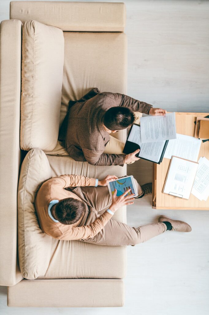 Young brokers sitting on couch in office and working with financial information